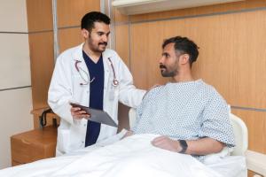 A KFSH physician holding a tablet and speaking with a patient sitting in a hospital bed