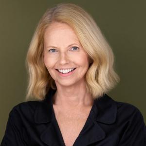 Professional headshot of a smiling blonde woman wearing a black blouse against an olive-green background.