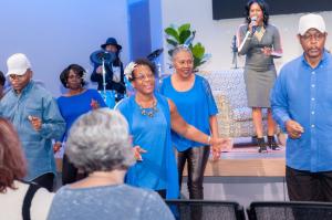 Myra Jones & The Soul Inspirational Line Dancers perform a choreographed dance in the foreground while Gospel singer Karla Nivens sings in the background.