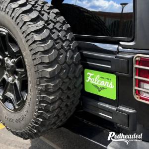 Bright green Oak Park Falcons team sign featuring white script lettering and a black falcon logo, mounted on the rear of a black off-road vehicle beside a large spare tire.