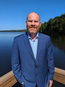 Chris Greene, Founder of The Flood Insurance Guru, in a blue blazer outdoors by a lake.