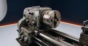Headstock and chuck of a used manual lathe on a navy backdrop