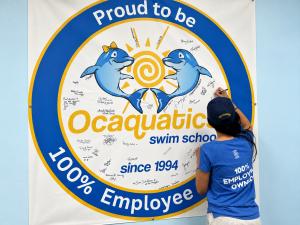 Ocaquatics team member signing the Employee Ownership Trust (EOT) banner during Employee Ownership Month.