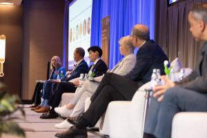 Moderator with five panelists seated on a stage