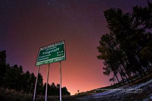 A green Flagstaff city limits sign proudly displaying its International Dark Sky City designation beneath a star-filled night sky.
