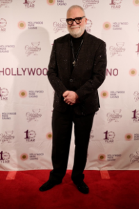 Jon Stetson in a dark suit and glasses poses on the Hollywood Park Casino red carpet.