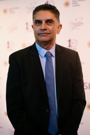 Deven Kumar in a suit and blue tie in front of the Hollywood Park Casino backdrop.