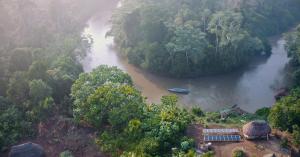 Aerial view of a solar-powered boat on a forest-lined river, with solar panels beside riverside buildings in Ecuador.