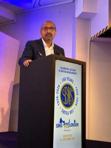 Dr. Mohana Rao Patibandla standing at the podium during the SBNS100 centenary meeting in London in October 2026.