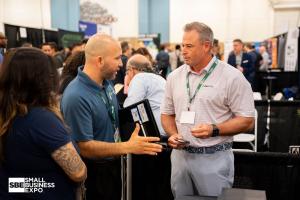 Two men and a woman talk on the exhibit floor at a previous Small Business Expo, surrounded by other attendees.