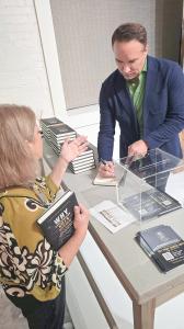 Johnathan H. Miller signing a copy of Why Underpricing Kills Design for a reader holding the book, with stacks of the book on the table