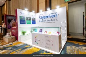 White Tyemvers corner booth with illuminated branding, glass product showcases, a reception counter and brochure rack.