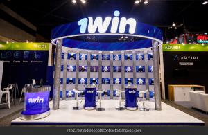 Blue and white 1win booth with a curved illuminated header, a grid of figurine displays and cylindrical meeting counters.