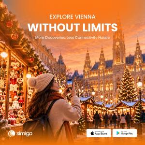 A traveler taking a smartphone photo at Vienna’s Christmas market, surrounded by festive stalls, Christmas lights, and the illuminated Vienna City Hall, with Simigo branding.