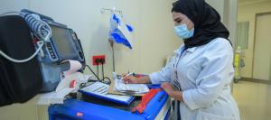 A KFSH nurse documenting patient care at the bedside in a hospital room