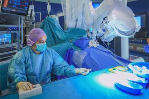 A KFSH surgical team member preparing instruments beside a robotic surgical system in an operating room