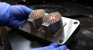 Person holds a silver-coloured metal model component with two circular tubes that have bronze-coloured, root-like metal print inside.