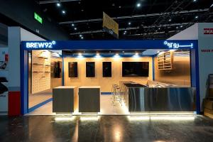 BREW92 coffee exhibition booth with blue fascia, wood wall panels and steel counters.