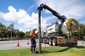 Pulse Locating operator guiding the vacuum hose into the ground beside the truck, with traffic cones behind