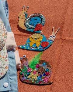 Children craft wooden snails with paint, jewels, foam stickers, googly eyes and feathers. inspired by picture book, Carrie the Tree Fairy.