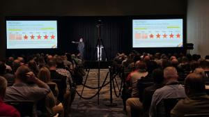 West is on the stage with a side showing how "increasing the clarity in which we describe cybersecurity risk management" is able to address problems.