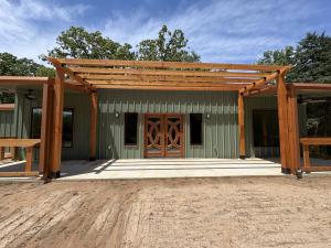 Green metal-sided custom barndominium with timber pergola and double wood entry doors in East Texas