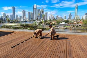 Altar Decks team restoring timber decking on a Gold Coast commercial balcony with city skyline.