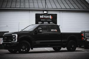 Camionnette noire avec le logo de Béton SD stationnée devant un bâtiment portant l’enseigne de l’entreprise