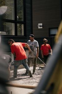 Équipe de quatre ouvriers de Béton SD qui étalent du béton frais avec des règles devant une maison moderne