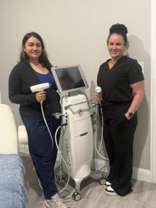 Two women from the Nuvia Aesthetics team in black scrubs standing on either side of a white Candela Matrix device, each holding a treatment handpiece.