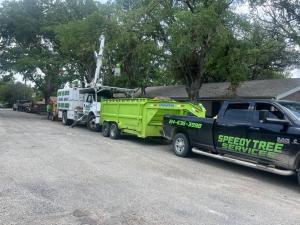 Speedy Tree Services bucket truck, dump trailer and pickup parked along a street