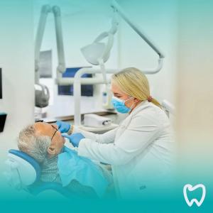 Dentist in mask examining an older patient's teeth in treatment chair at Smile Dental Care