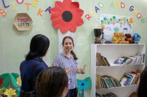 A woman in a blue and white striped shirt speaks with visitors inside a colourful children’s education centre in Timor-Leste, with bookshelves, toys and children’s artwork in the background.