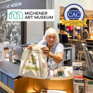 Smiling museum staff member displays a Micherner Art Museum sensory kit bag at the welcome desk.