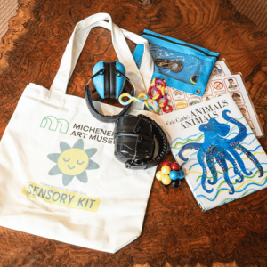 Sensory kit with a museum tote bag, headphones, fidget toys, colorful charms, and an illustrated “Animals Animals Animals” book.
