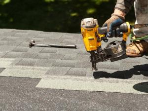 Roofer's gloved hand nailing asphalt shingles with a pneumatic roofing nailer