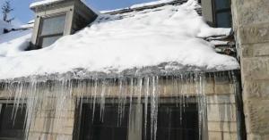 Heavy snow on a roof with long icicles hanging from the gutter line of a stone house