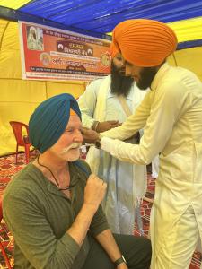 Two Sikh men assist Chip Walter by wrapping a blue turban around his head in a yellow tent.