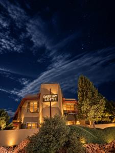 Illuminated exterior of Dark Sky Lofts in Sedona, Arizona, featuring Southwestern architecture, landscaped grounds, and a glowing property sign beneath a star-filled night sky with wispy clouds.
