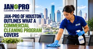 A uniformed JAN-PRO Cleaning & Disinfecting professional wiping a conference room table in a modern Houston office, with the city skyline in the background, illustrating recurring commercial cleaning and janitorial services.
