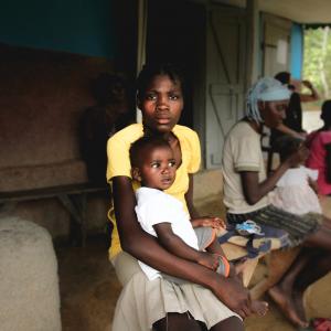 A mother sits on a wooden bench holding her child at a clinic in Haiti.