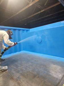 Applicator spraying polyurea inside a shipping container pool