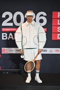Model wearing Tal Zohar’s RLSD 2026 winning design, featuring a white quilted leather jacket with contrasting piping, pleated leather skirt, white visor and vintage wooden tennis racket, against the branded Bangkok competition backdrop.