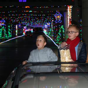 Two kids enjoying the lights as they eat popcorn and watch the show - popping out of the sunroof of their vehicle as it slowly makes its way through one of the light tunnels at Glittering Lights