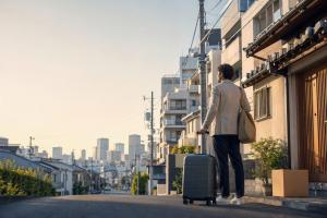 International newcomer carrying a suitcase along a Tokyo residential street, representing moving to Japan, finding housing and planning living costs.