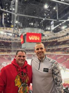 Jeff Nydegger and fellow Army veteran Chris smiling together inside a Chicago hockey arena, with the ice rink and stadium seating in the background.
