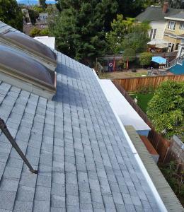 Newly installed grey asphalt shingle roof with skylights and seamless white rain gutters on a Bay Area home.