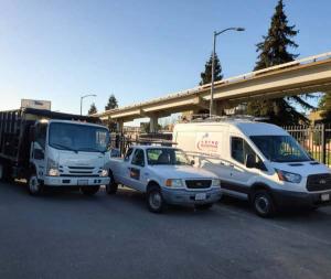 Fleet of Astro Roofing Inc. work trucks and branded service van parked on-site in Oakland, California.