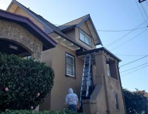 Astro Roofing technician using a ladder to perform gutter installation service on a multi-story Oakland home.