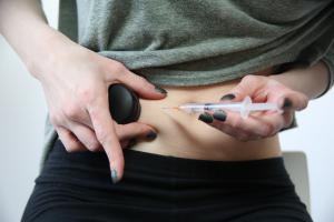 Woman using Buzzy while self-injecting medicine into her stomach